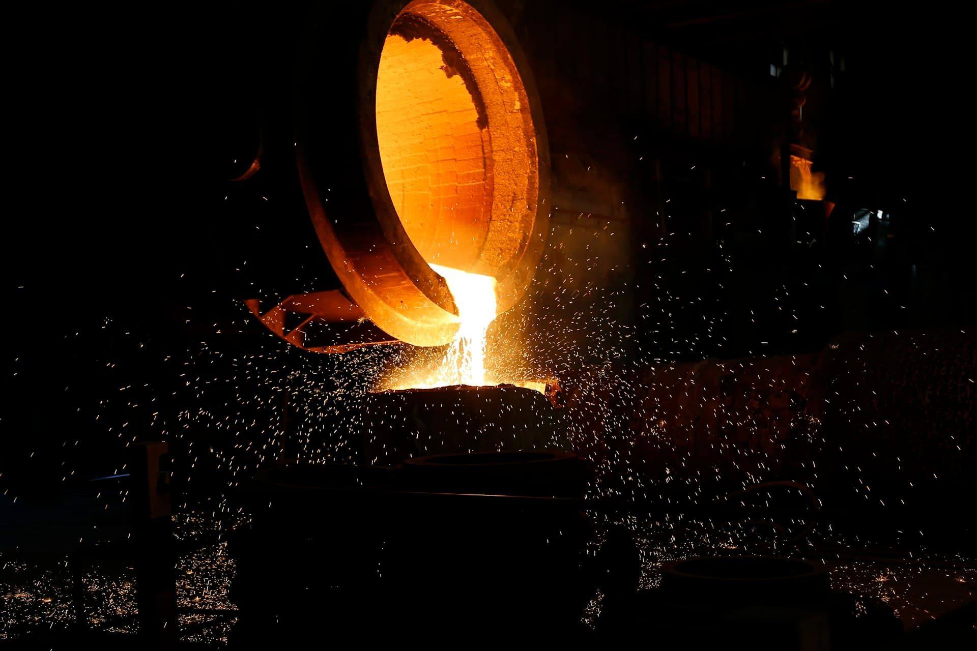 Molten metal pouring from a furnace ladle in a foundry, sparks flying